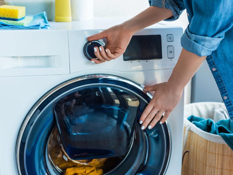 Frauenhände schließen Waschmaschine und stellen Waschprogramm ein