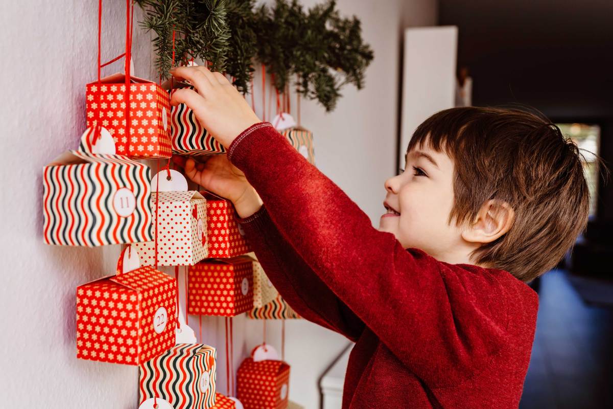 Kleiner Junge schaut vorsichtig in ein Kalendertürchen seines Adventskalenders.