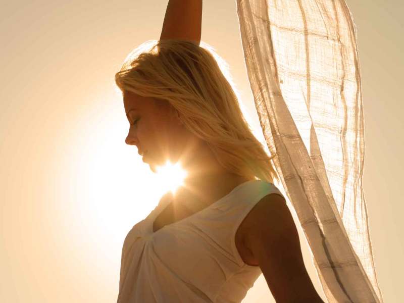 Frau steht in der Sonne und hält ein Tuch hoch.