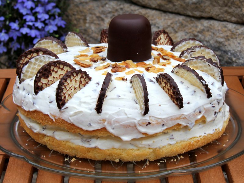 Torte mit Creme und Schokoküssen auf einem Kuchenteller.