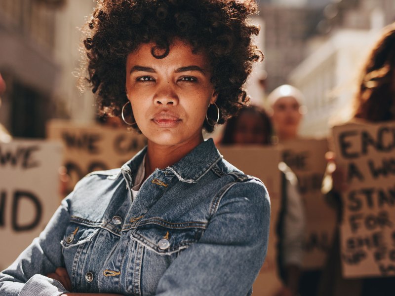 Schwarze Frau mit verschränkten Armen auf einer feministischen Demo.