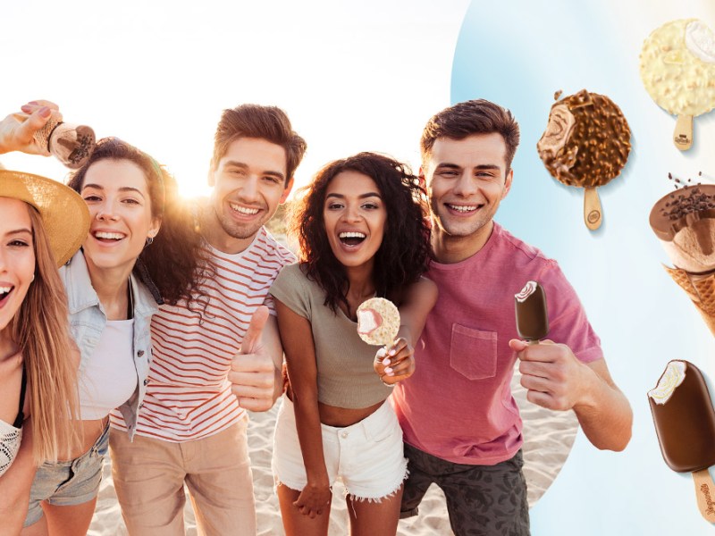 Eine fröhliche Gruppe junger Menschen posiert lachend am Strand, mit schwebenden Eisvariationen im Vordergrund.