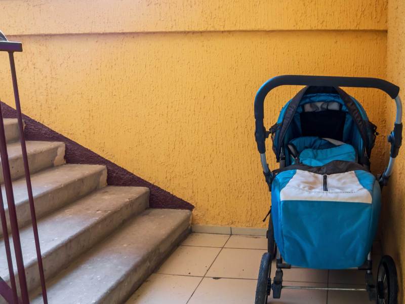 Bild eines Kinderwagens der am Fuße einer Treppe eines Wohnhauses steht.