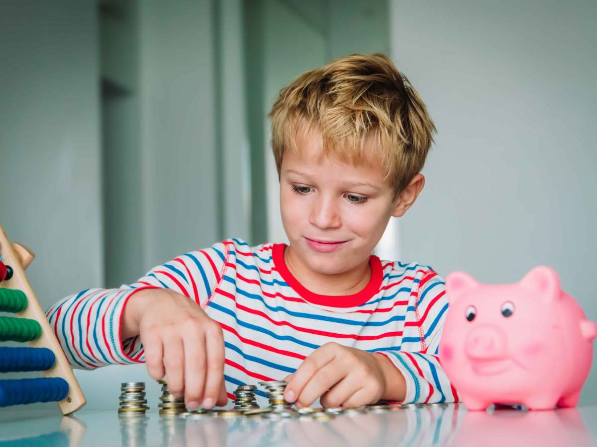 Junge, ca. 8 Jahre, zählt sein Taschengeld. Auf dem Tisch stehen außerdem ein Sparschwein und ein Rechenschieber.