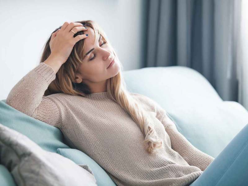 Frau liegt erschöpft auf der Couch und kann nicht mehr arbeiten.