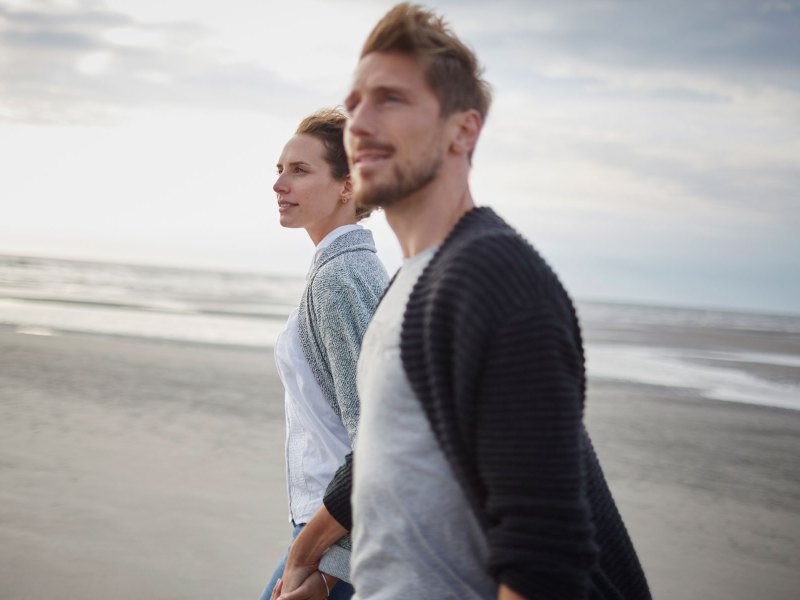 Ein Paar läuft Hand in Hand über den Strand.