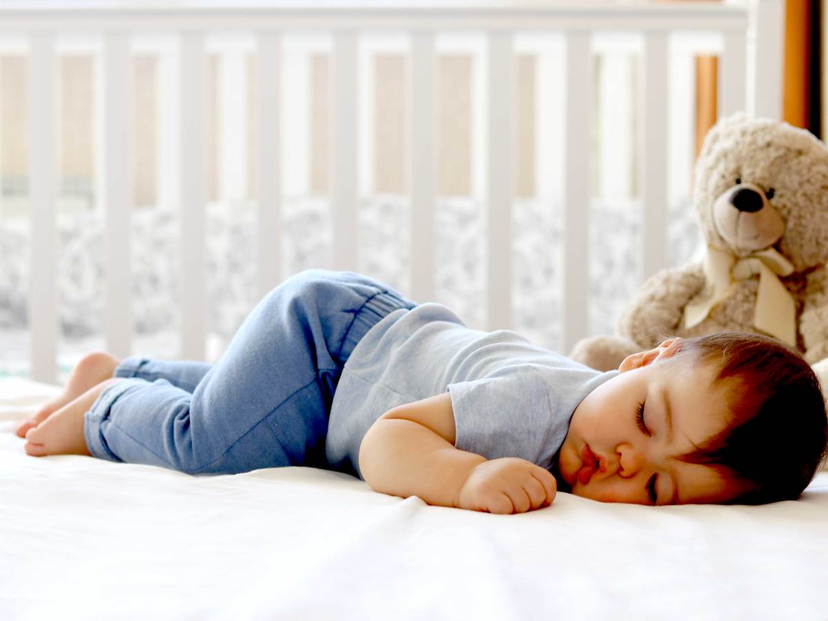 Kleinkind liegt auf dem Bauch im Elternbett und schläft tief und fest.