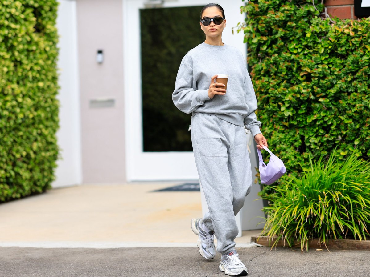 Frau mit grauen Outfit aus Sweater und Jogginghose und Sneaker vor Hecke