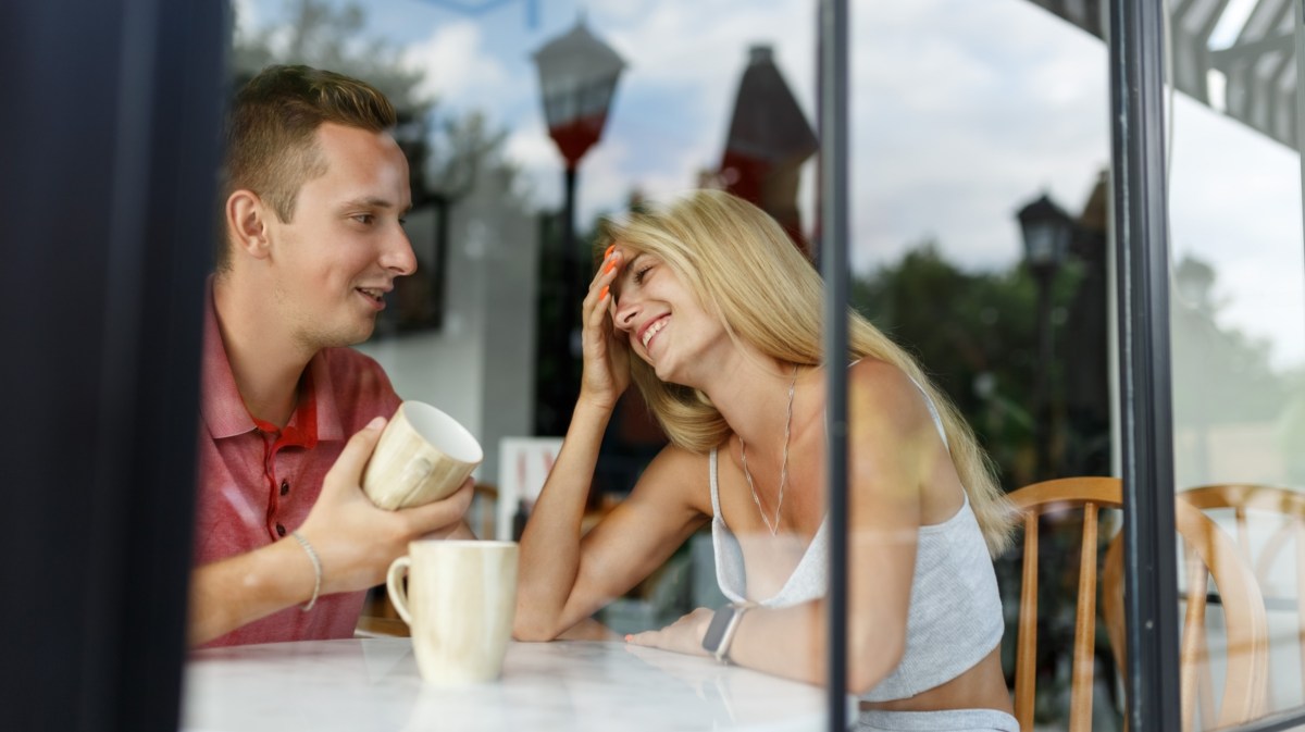 Frau und Mann hinter Glasscheibe, die lachen und einen Kaffee aus einer Tasse trinken