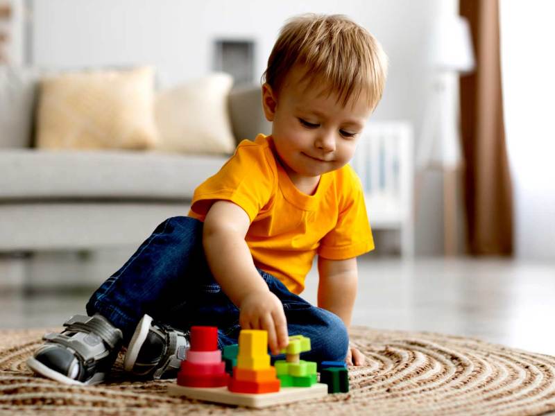 Kleiner Junge, ca. zwei oder drei Jahre, sitzt auf dem Boden und spielt mit Holzbausteinen.
