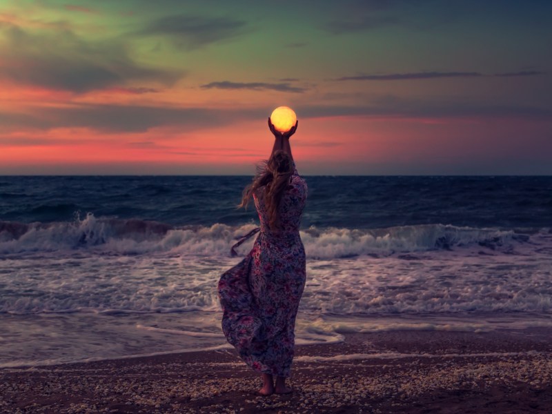 Frau am Strand, die mit ihren Händen den Mond in ihren Händen hält