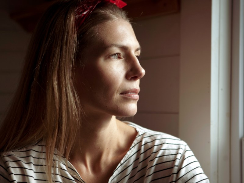 Frau schaut nachdenklich aus dem Fenster.