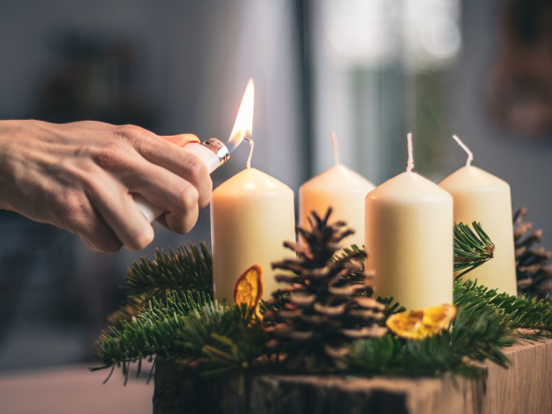 Eine Kerze auf einem Adventskranz wird mit einem Feuerzeug angezündet.
