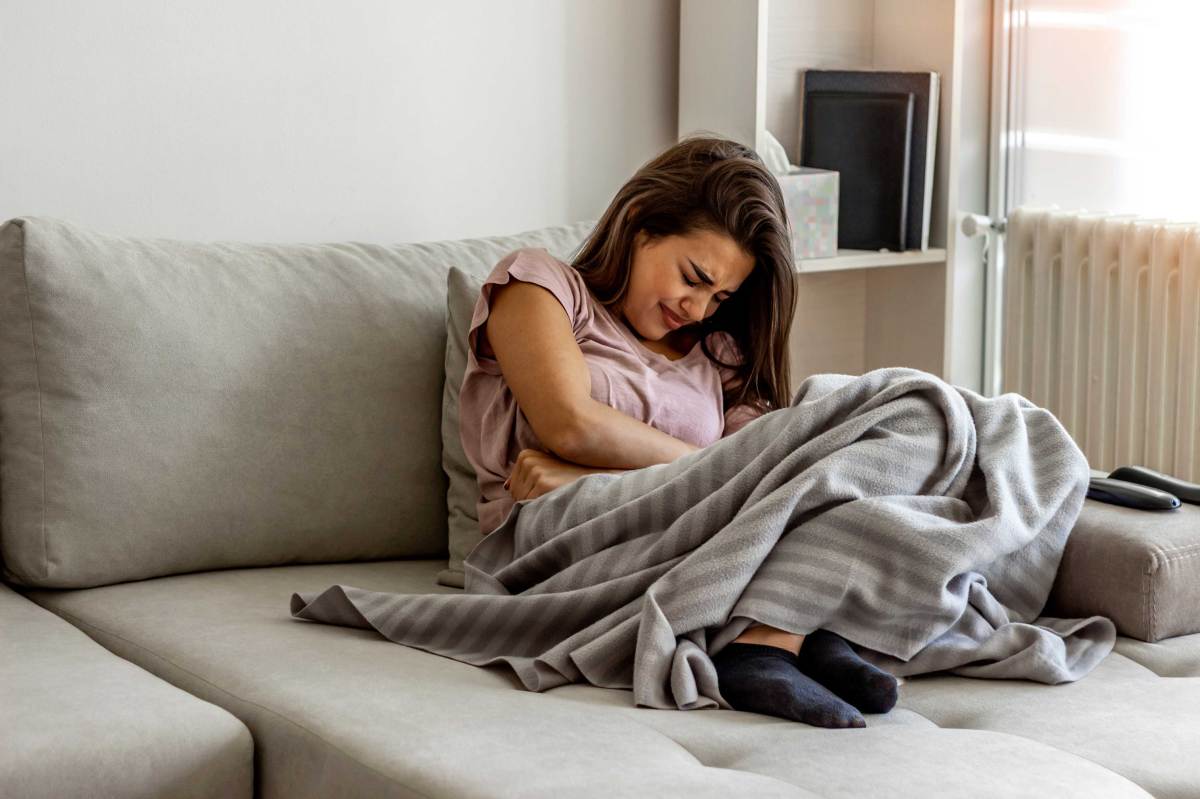 Frau mit Bauchschmerzen leigt auf Sofa