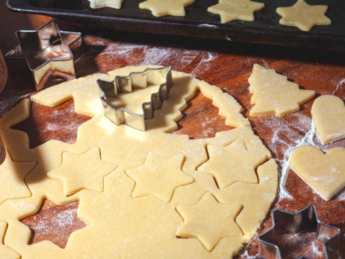 Plätzchenteig auf Holztisch mit Ausstechformen.