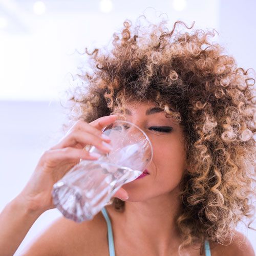 Frau mit Locken trinkt aus einem Wasserglas