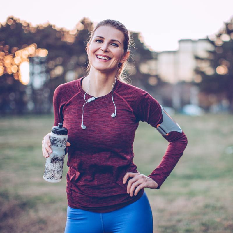 Frau in Sportkleidung steht in der Natur und lächelt