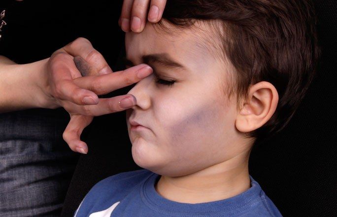 Junge bekommt mit dunklem Make-up Schatten unter die Augen und auf die Wangenknochen gemalt.