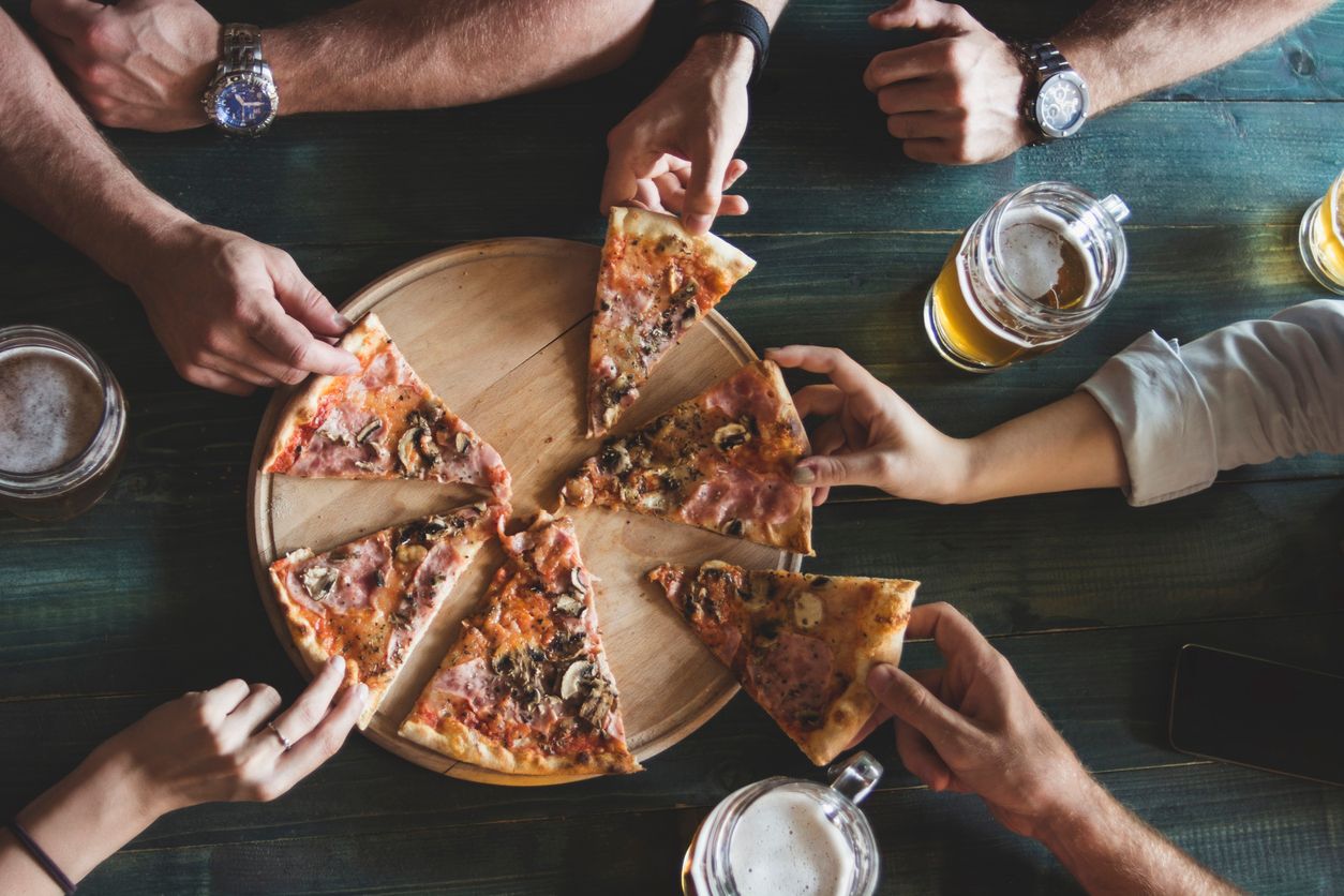 Beim gemeinsamen Abendessen, zu sehen sind mehrere Hände, die nach je einem Stück Fertigpizza greifen.