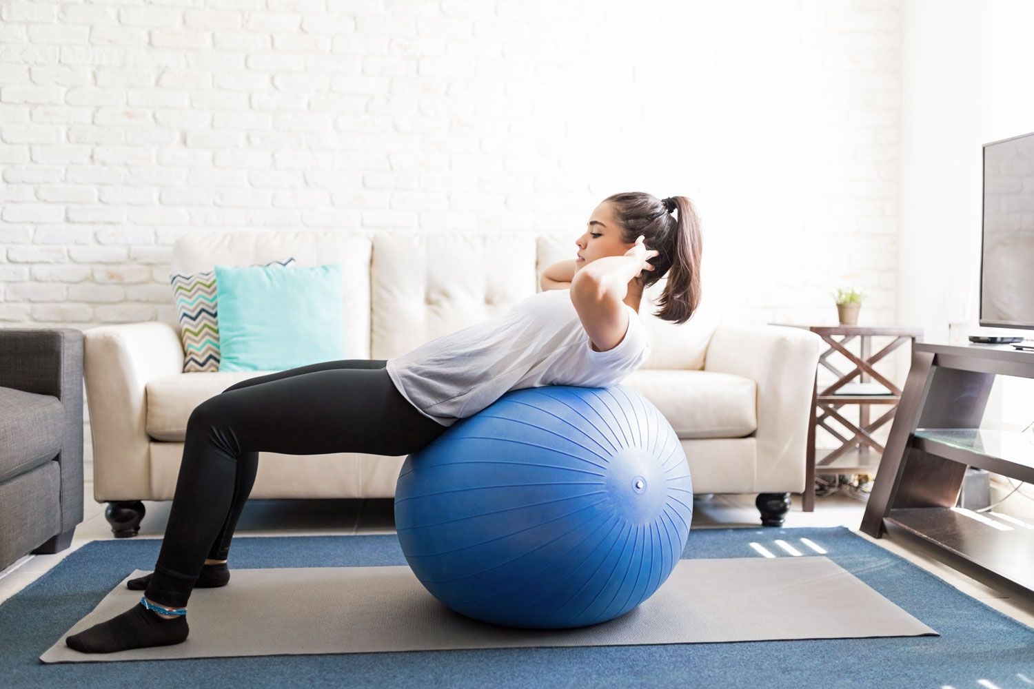 Junge Frau trainiert mit blauem Ball in ihrem Wohnzimmer. 