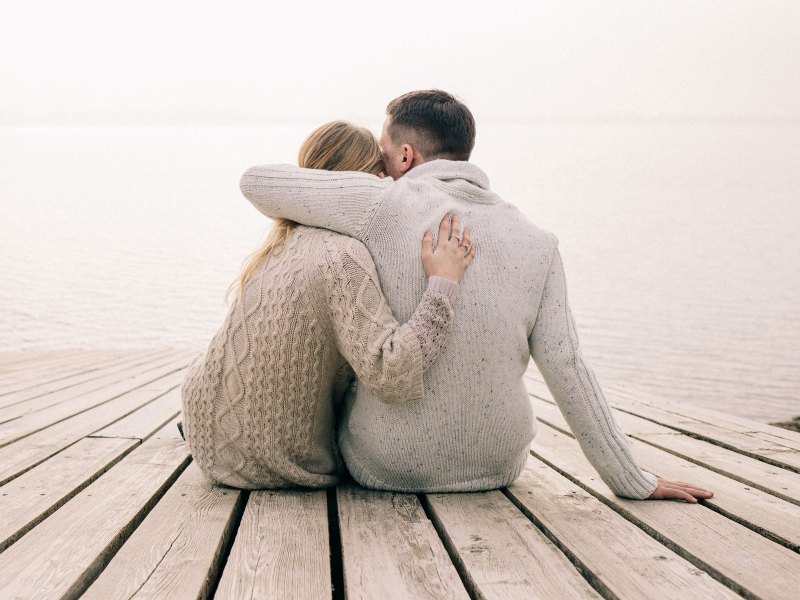 Paar sitzt Arm in Arm an einem See.