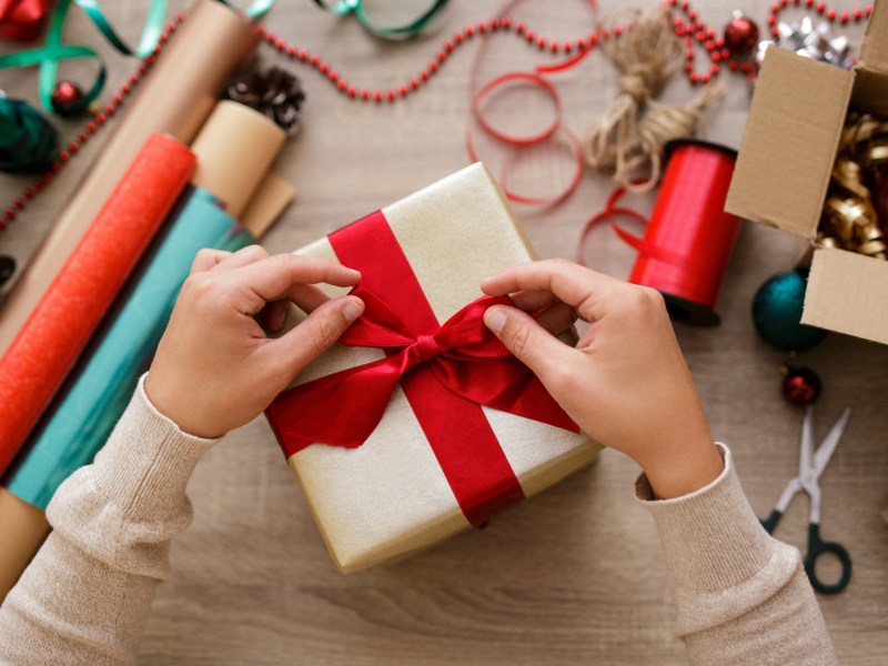 Eine Frau verpackt ein Geschenk in Geschenkpapier und bindet eine Schleife darum.
