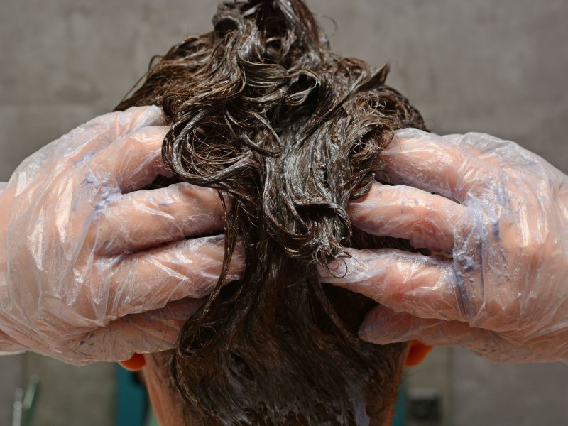 Frau, die sich gerade die Haare mit Coloration färbt.