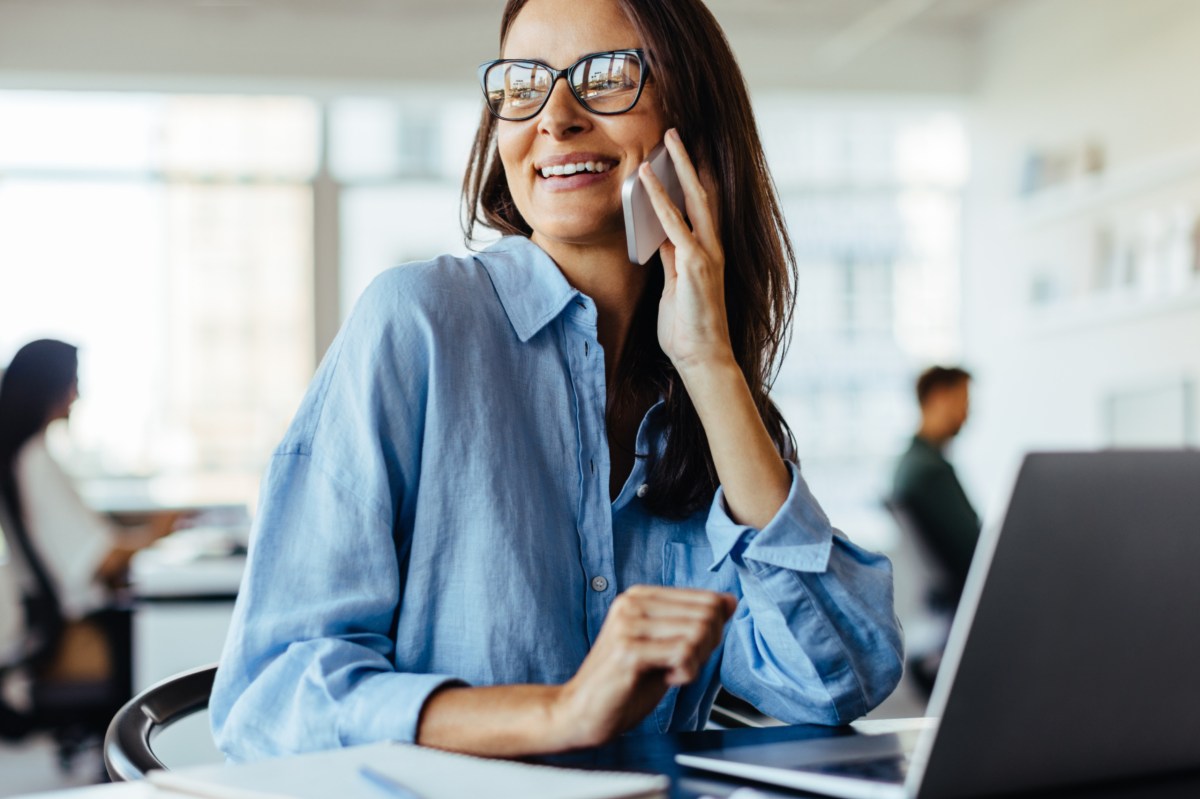 Frau am Arbeitsplatz hat ein Handy in der Hand und telefoniert.