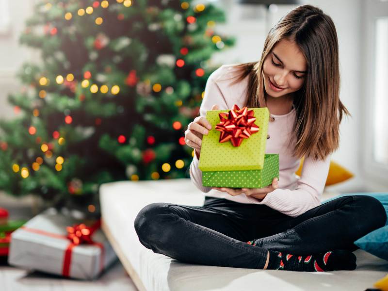 Teenager-Mädchen schaut neugierig in ein Weihnachtsgeschenk.