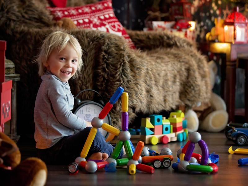 Kleiner Junge spielt in einem winterlich und gemütlich eingerichteten Wohnzimmer mit seinen magnetischen Bausteinen.