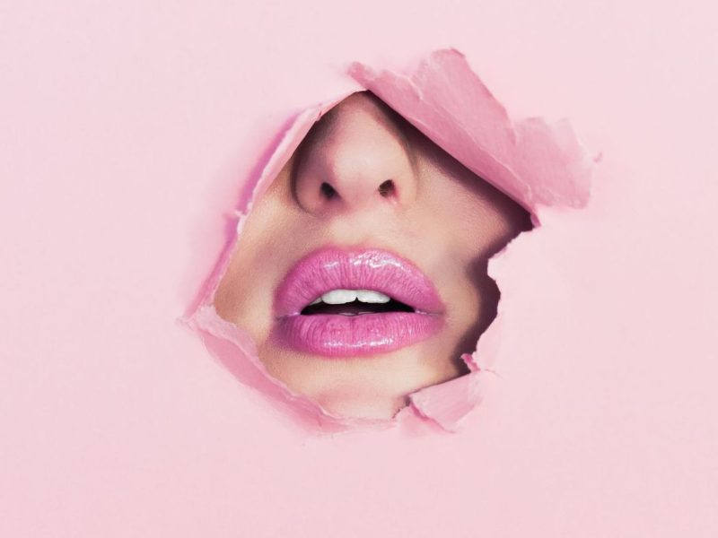Teil eines weiblichen Gesichts ist durch Loch in rosa Wand zu sehen