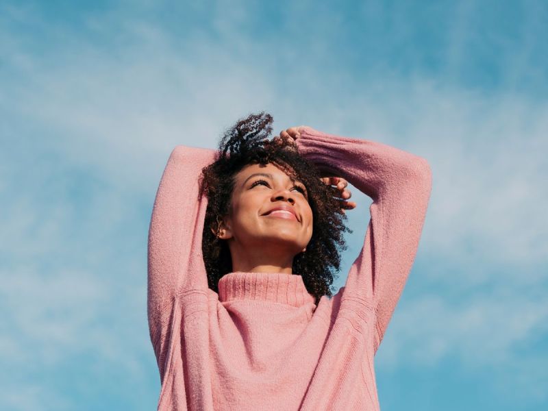 Junge Frau in rosa Pullover ist gut gelaunt, fröhlich und blickt in den Himmel