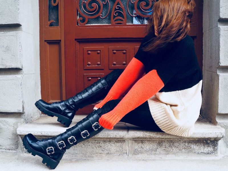 Symbolbild für Stiefel putzen: Frau trägt schwarze Stiefel und rot, schwarz, beiges Kleid