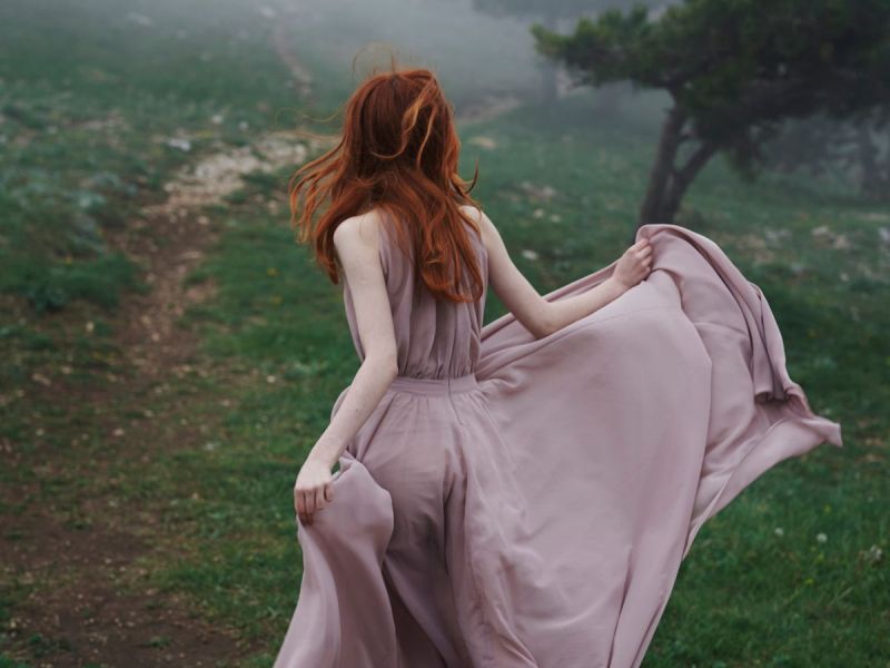 Eine Frau in einem weiten rosa Kleid läuft über eine Wiese