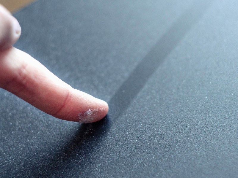Eine Person fährt mit dem Finger über eine staubige Oberfläche.