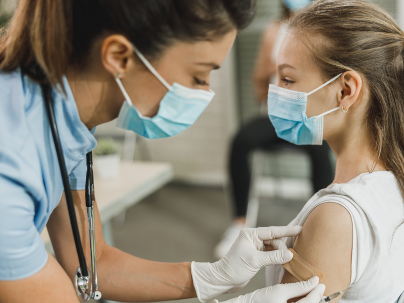 Ärztin mit Maske, die einem jungen Mädchen ein Pflaster nach der Impfung draufklebt