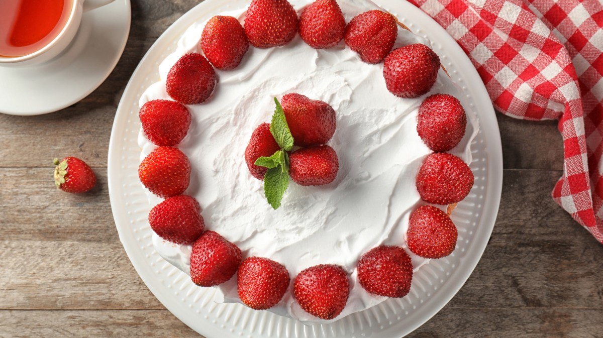 Kuchen mit Sahne und frischen Erdbeeren auf Holztisch.