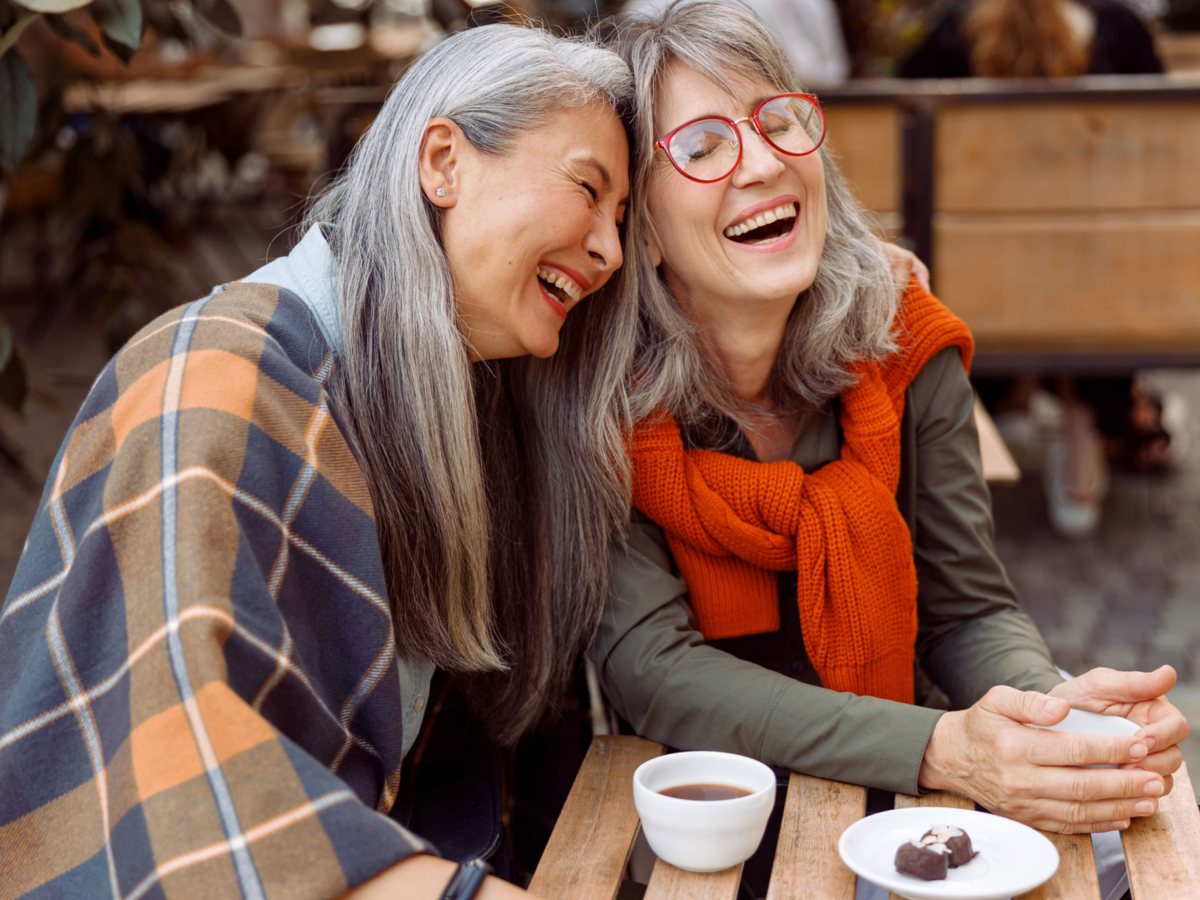 Zwei ältere Frauen sitzen in Café und lachen gemeinsam.