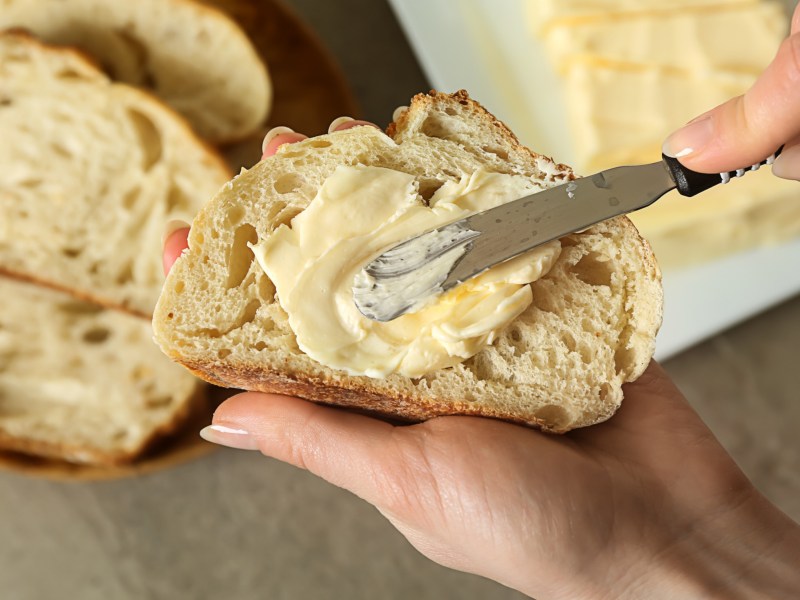 Person schmiert Butter oder Margarine auf eine Scheibe Brot.