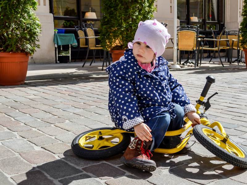 Kind sitzt trotzig auf seinem Laufrad mitten in der Stadt.