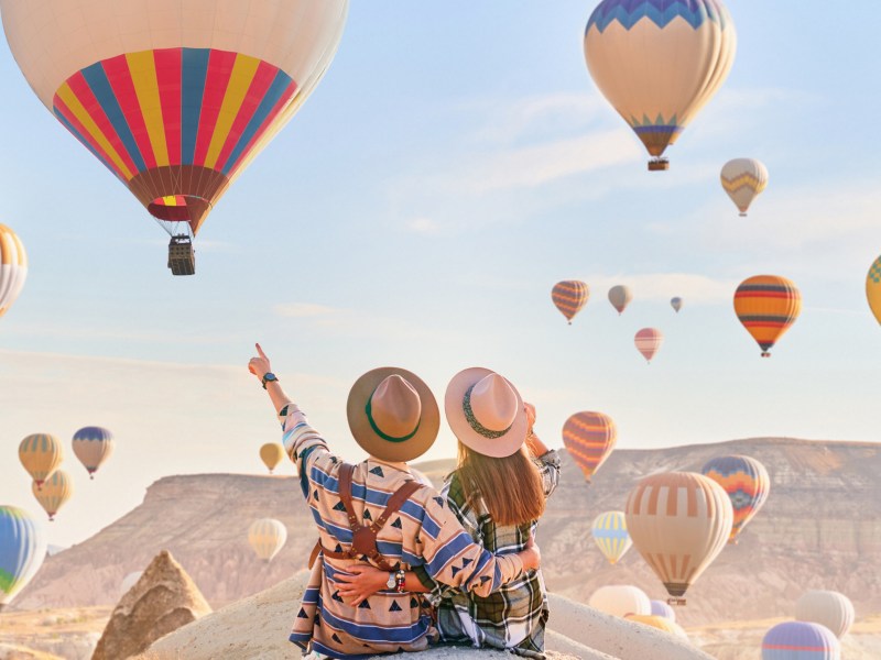 Frau und Mann auf einem Felsvorsprung umgeben von Heißluftballons