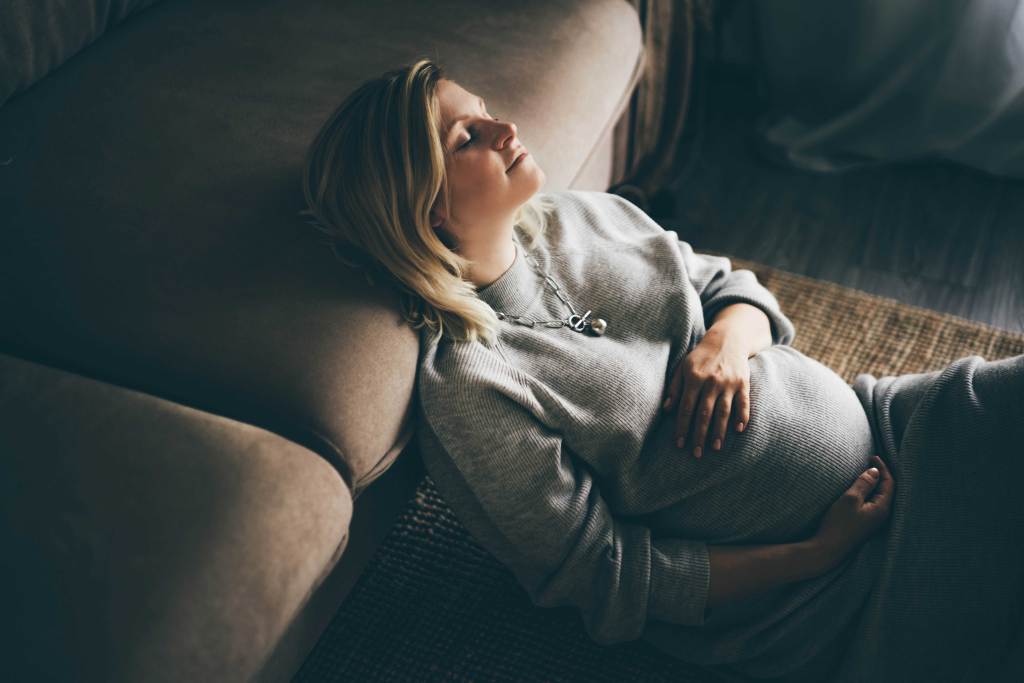 Schwangere Frau liegt im Wohnzimmer und entspannt
