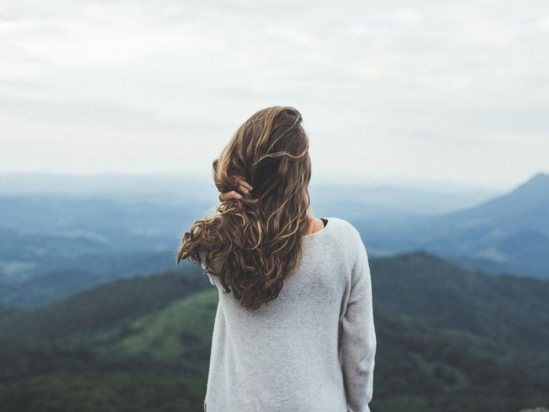 Junge Frau steht allein vor einer Landschaft.
