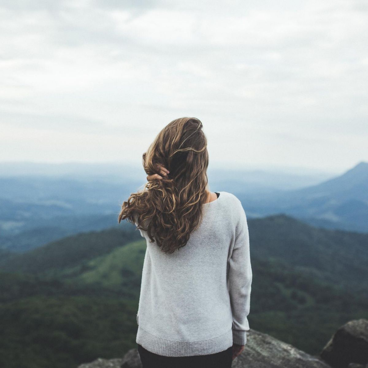 Junge Frau steht allein vor einer Landschaft.