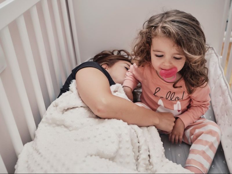 Mutter liegt neben Kleinkind, das wach im Bett sitzt