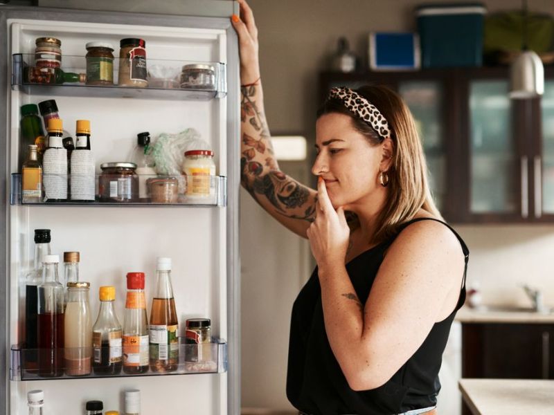 Frau steht am Kühlschrank und überlegt, was sie essen möchte