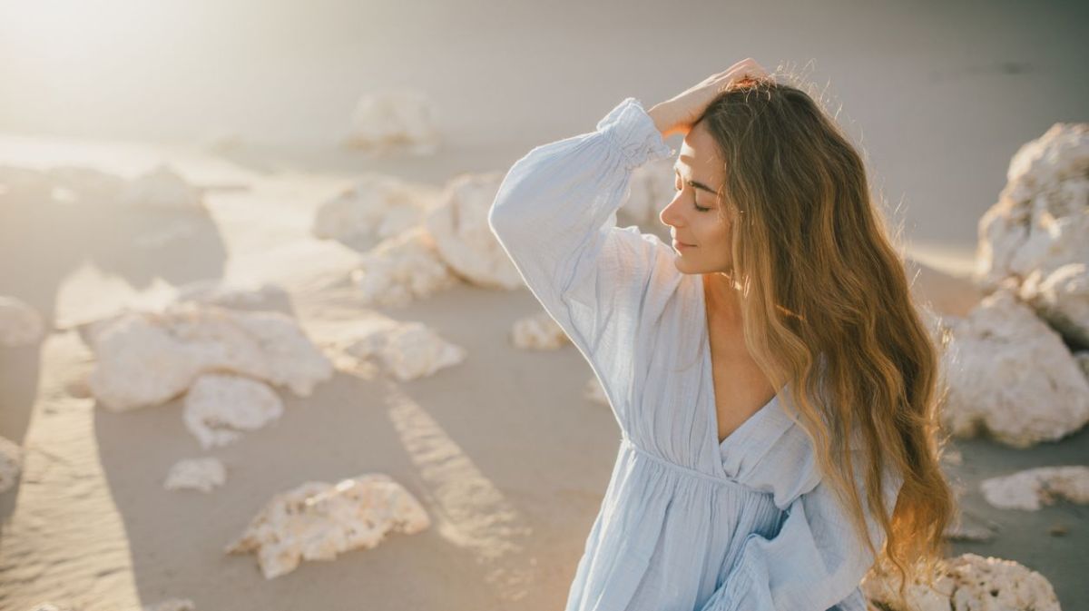 Frau bei Sonnenschein am Strand, die sich lässig durch die Haare geht 