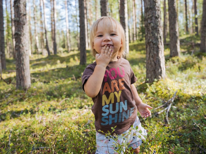 Blondes Baby, das im Wald steht und Beeren pflücken und isst