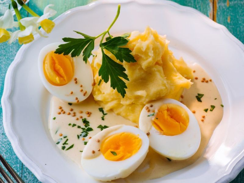 Hart gekochte Eier mit Senfsoße und Kartoffelpüree auf weißem Teller.