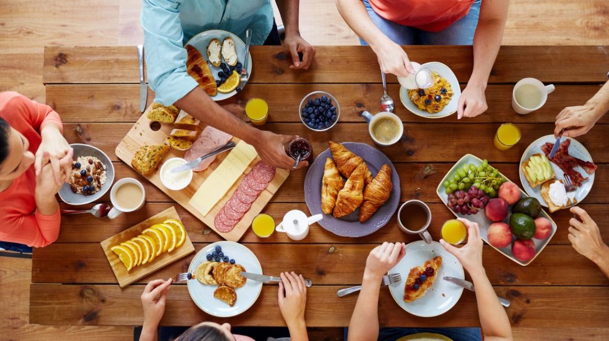 Eine Gruppe von Menschen sitzt gemeinsam am Tisch und frühstückt zusammen